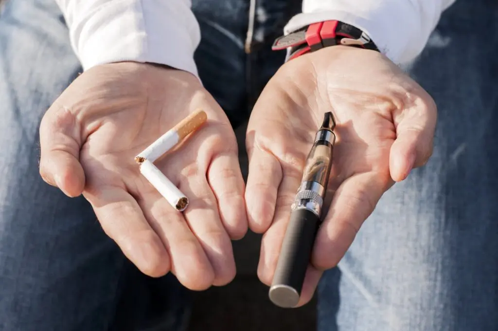 Vaping vs smoking — broken cigarette and vape pen in hands