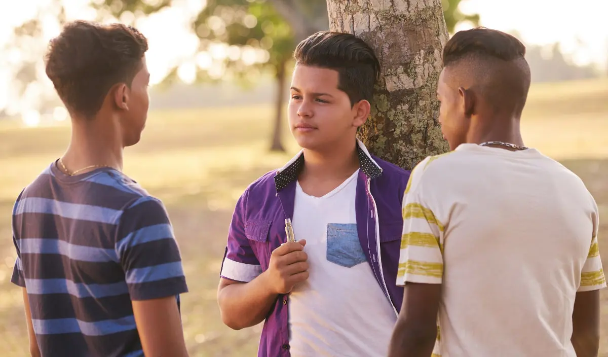 What Is the Legal Age to Buy a Vape in the U.S.? Group of Teens In Park Boy Smoking Electronic Cigarette
